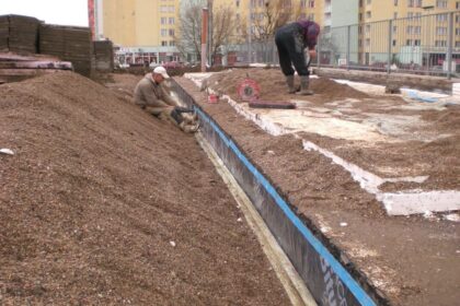 Pracownicy układają warstwę hydroizolacyjną na placu budowy.