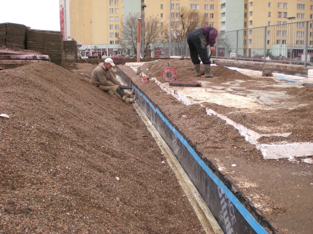 Pracownicy układają warstwę hydroizolacyjną na placu budowy.