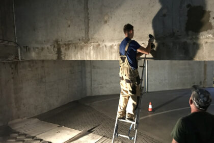 Mężczyzna na drabinie wykonuje iniekcje krystaliczne na betonowej ścianie.