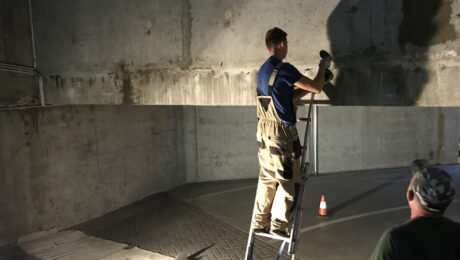 Mężczyzna na drabinie wykonuje iniekcje krystaliczne na betonowej ścianie.