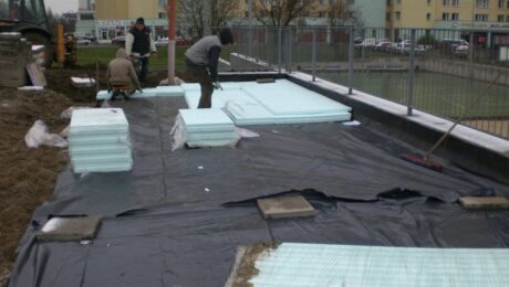 Robotnicy montują izolacje przeciwwilgociowe na placu budowy przed blokiem mieszkalnym.