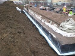 Pracownicy wykonują hydroizolacje na fundamentach budynku.