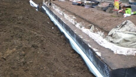 Pracownicy wykonują hydroizolacje na fundamentach budynku.