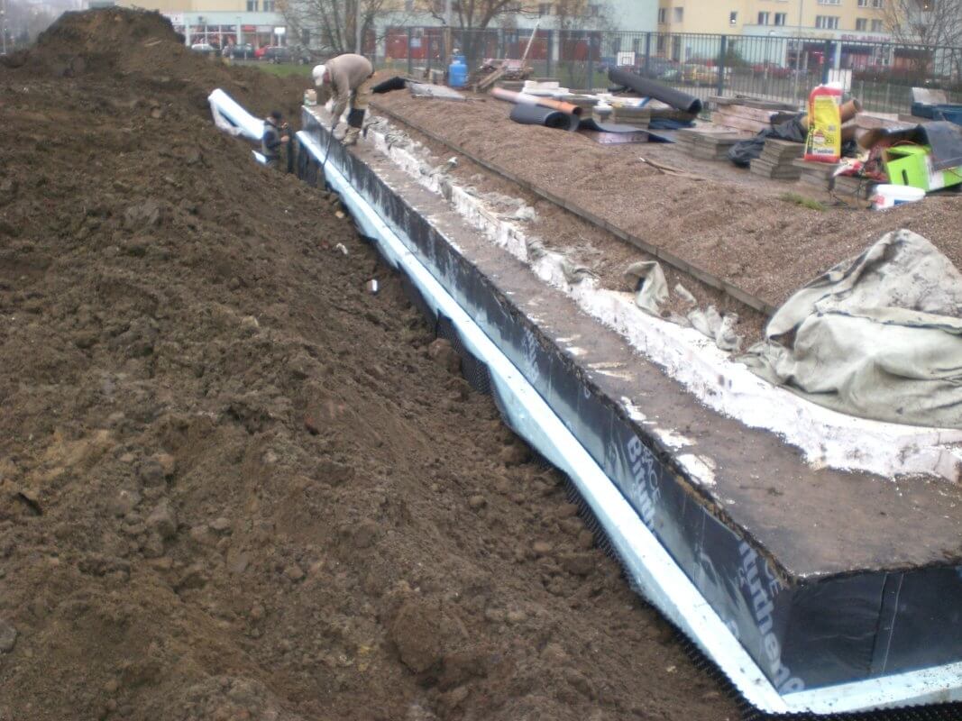 Pracownicy wykonują hydroizolacje na fundamentach budynku.