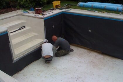 Dwóch mężczyzn pracuje nad montażem izolacji przeciwwodnej w pustym basenie.