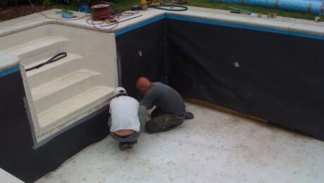 Dwóch mężczyzn pracuje nad montażem izolacji przeciwwodnej w pustym basenie.