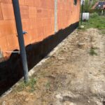 Ściana budynku z wyraźnie widoczną izolacją fundamentów w postaci ciemnej powłoki.