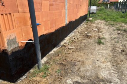 Ściana budynku z wyraźnie widoczną izolacją fundamentów w postaci ciemnej powłoki.