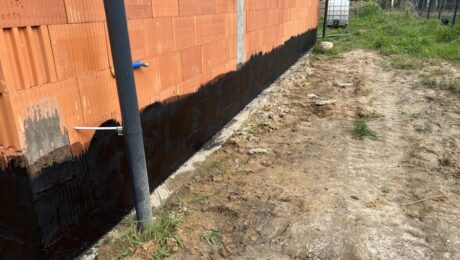 Ściana budynku z wyraźnie widoczną izolacją fundamentów w postaci ciemnej powłoki.