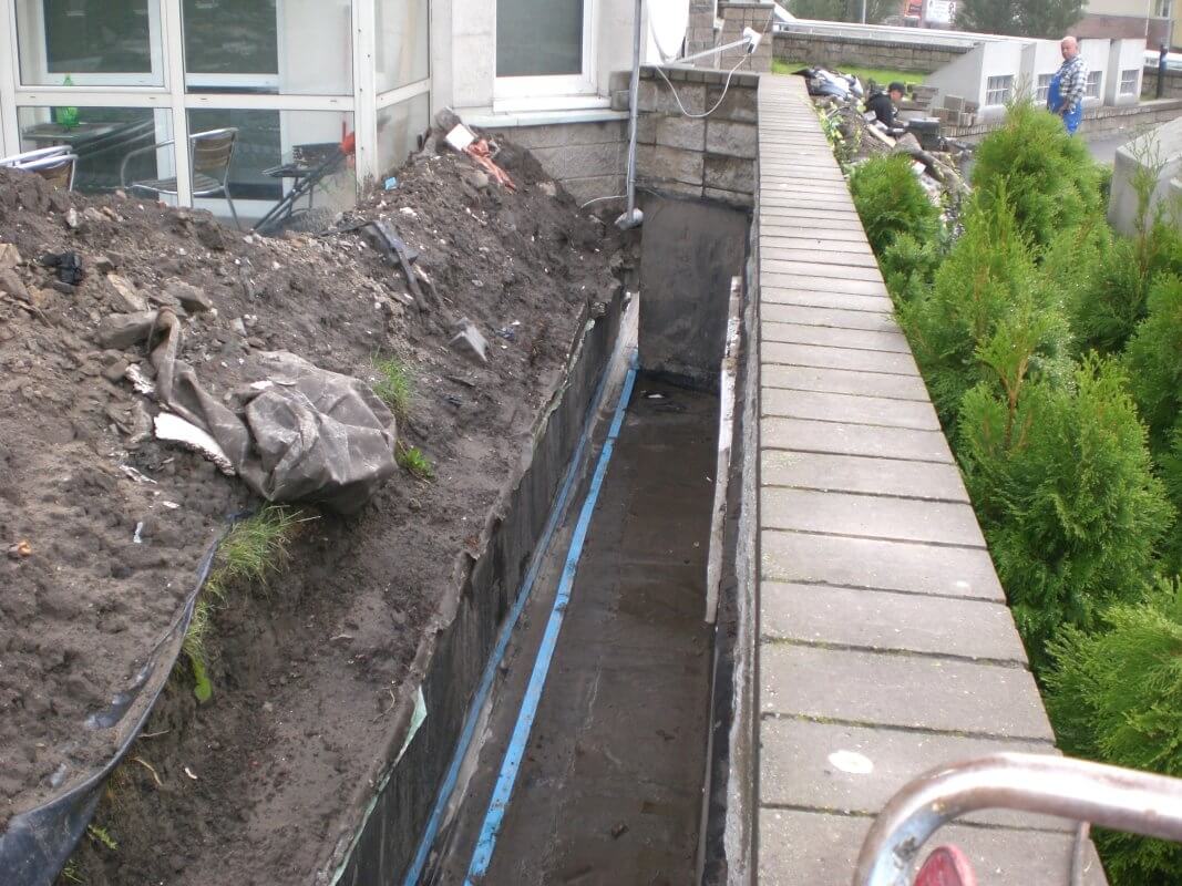 Prace związane z uszczelnianiem betonu przy ścianie budynku.