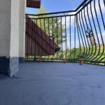Widok na świeżo wykonaną izolację balkonu z kutą balustradą na tle błękitnego nieba.