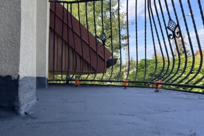 Widok na świeżo wykonaną izolację balkonu z kutą balustradą na tle błękitnego nieba.