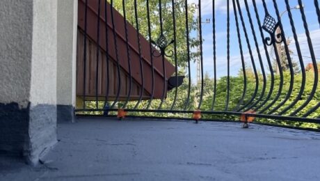 Widok na świeżo wykonaną izolację balkonu z kutą balustradą na tle błękitnego nieba.