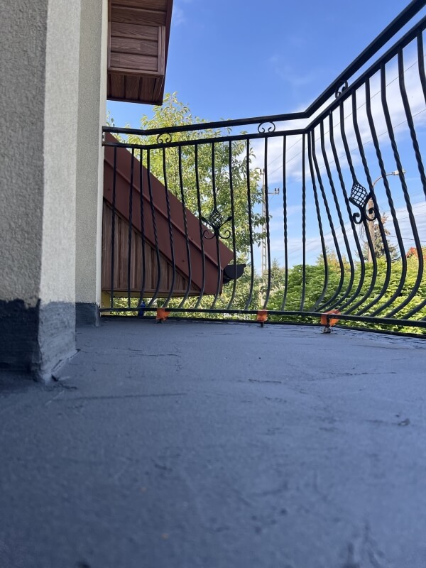 Widok na świeżo wykonaną izolację balkonu z kutą balustradą na tle błękitnego nieba.