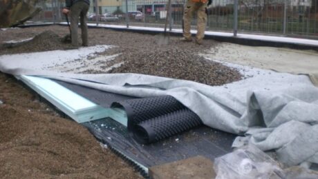 Robotnicy układają warstwy materiałów, w tym izolacje przeciwwilgociowe, na placu budowy.