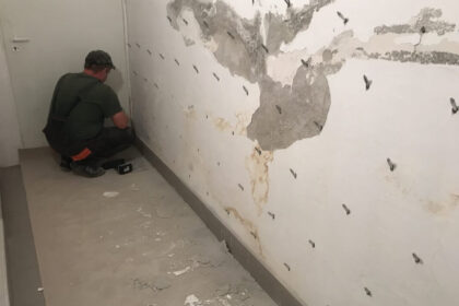 Mężczyzna pracuje nad ścianą, przygotowując ją do procesu iniekcji ciśnieniowej.