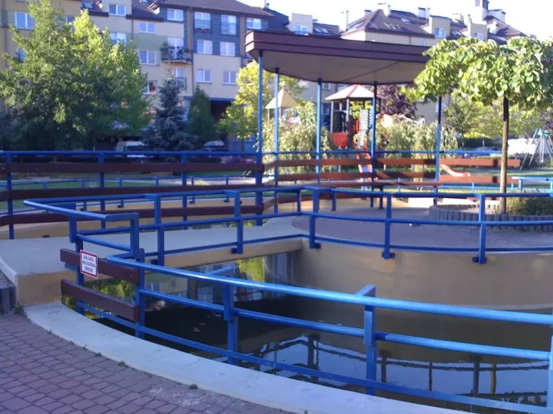 Zbiornik wodny przy placu zabaw na osiedlu, otoczony balustradą