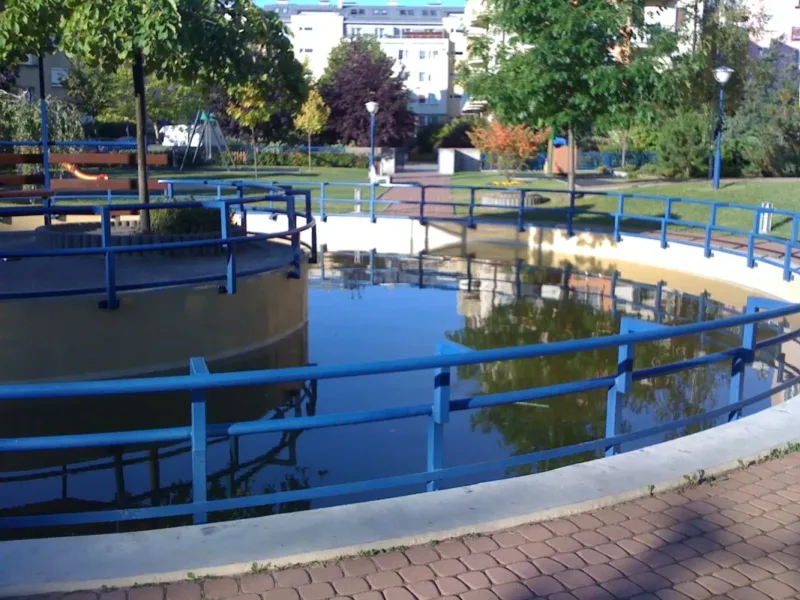 Ozdobny zbiornik wodny na terenie osiedla z niebieską balustradą