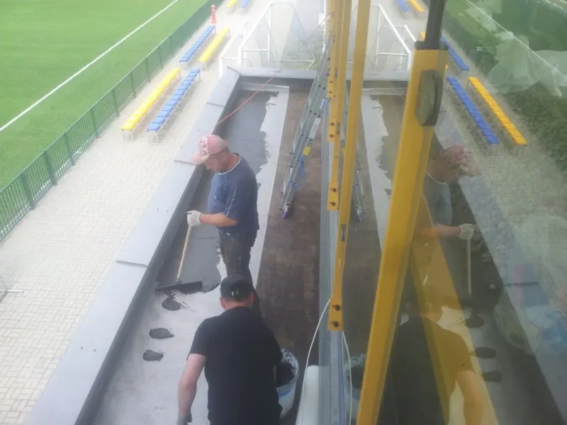 Pracownicy przy izolacji dachu trybuny nad boiskiem