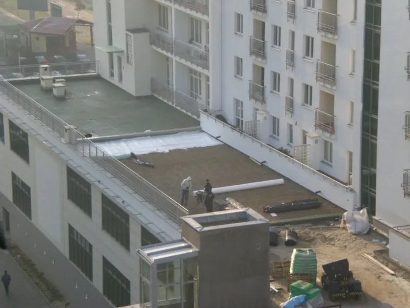 Układanie warstw tarasu na dachu niższego budynku przy wieżowcu