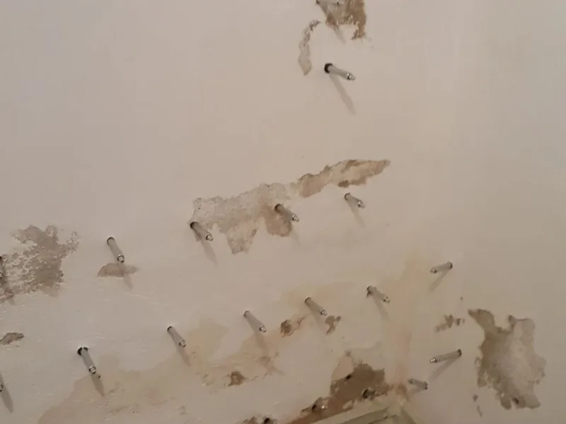 Narożnik pokoju z pakerami i ubytkami tynku, podłoga przykryta folią