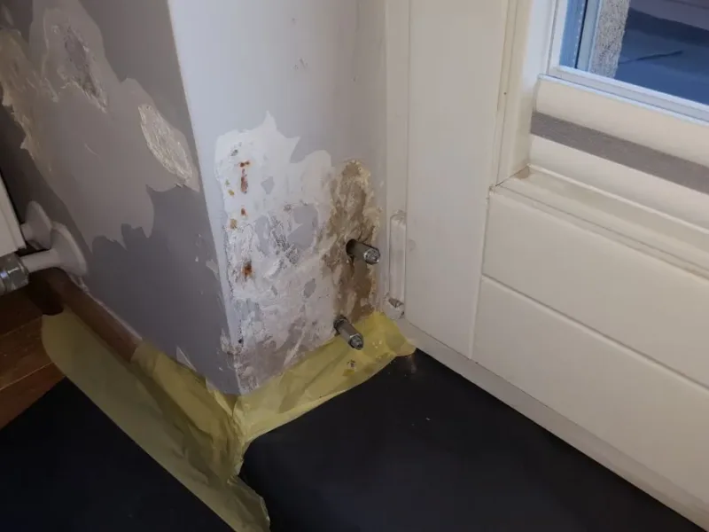 Zawilgocony narożnik przy oknie z pakerami, pod grzejnikiem taśma i folia ochronna