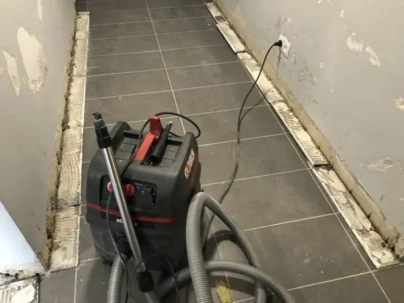 Korytarz z rozciętymi stykami posadzki i ścian, przy pracy odkurzacz przemysłowy