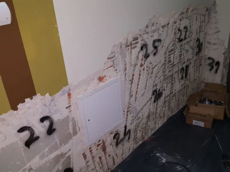 Ściana z odbitym tynkiem i numerami zapisanymi markerem, podłoga przykryta folią