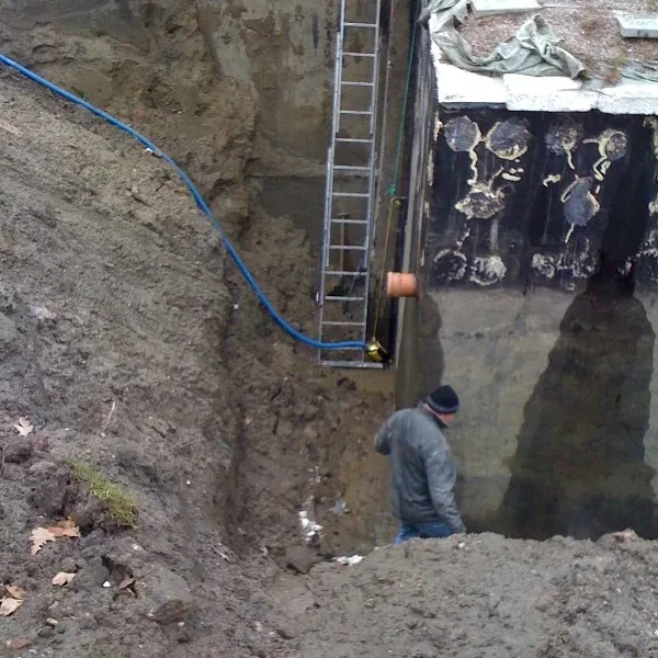Głęboki wykop przy ścianie fundamentowej z membraną, w wykopie pracownik i drabina