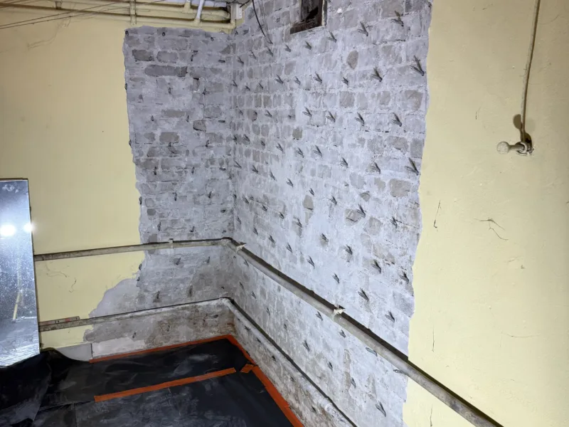 Piwnica w trakcie prac - odsłonięty mur z cegły i folia na posadzce