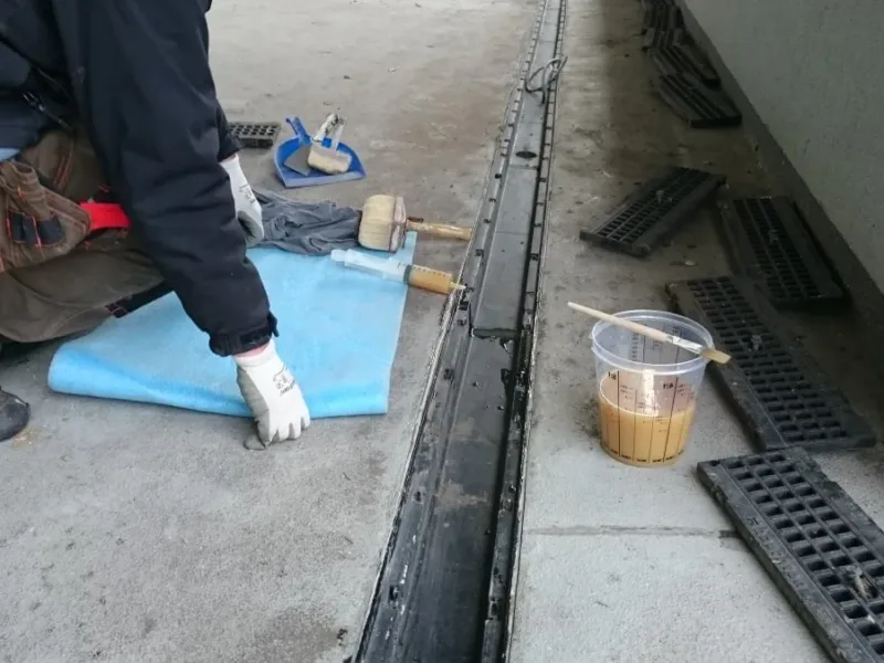 Wklejanie tkaniny wzmacniającej przy korytku odwodnienia, obok żywica w pojemniku