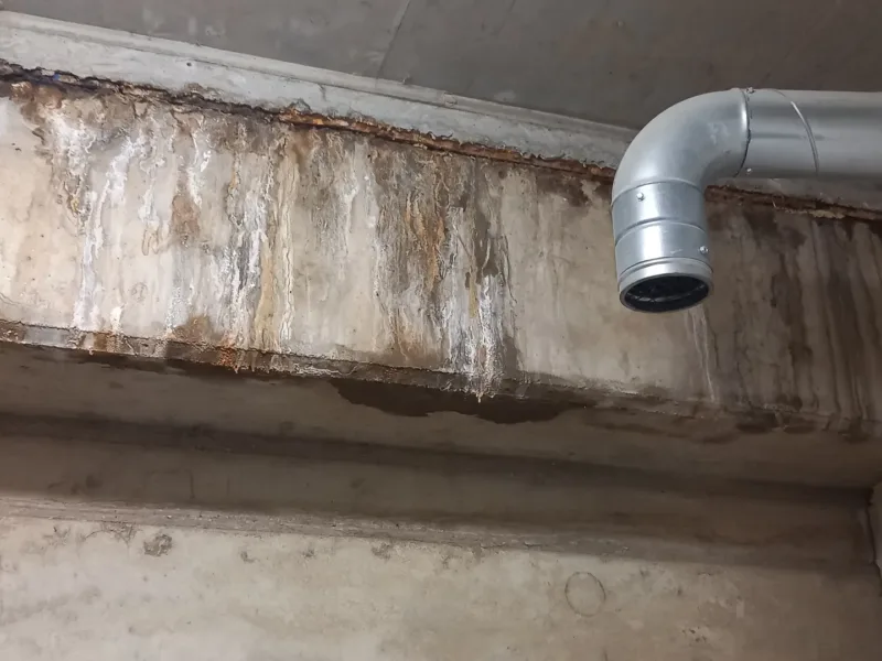 Zacieki i rdzawe plamy na stropie przy przejściu rury